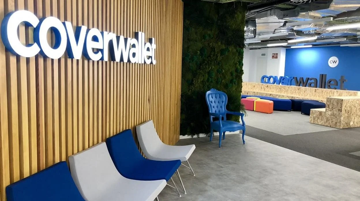 CoverWallet office entrance with illuminated logo on a slatted wooden wall, a blue accent chair and colourful seating in a modern workspace.