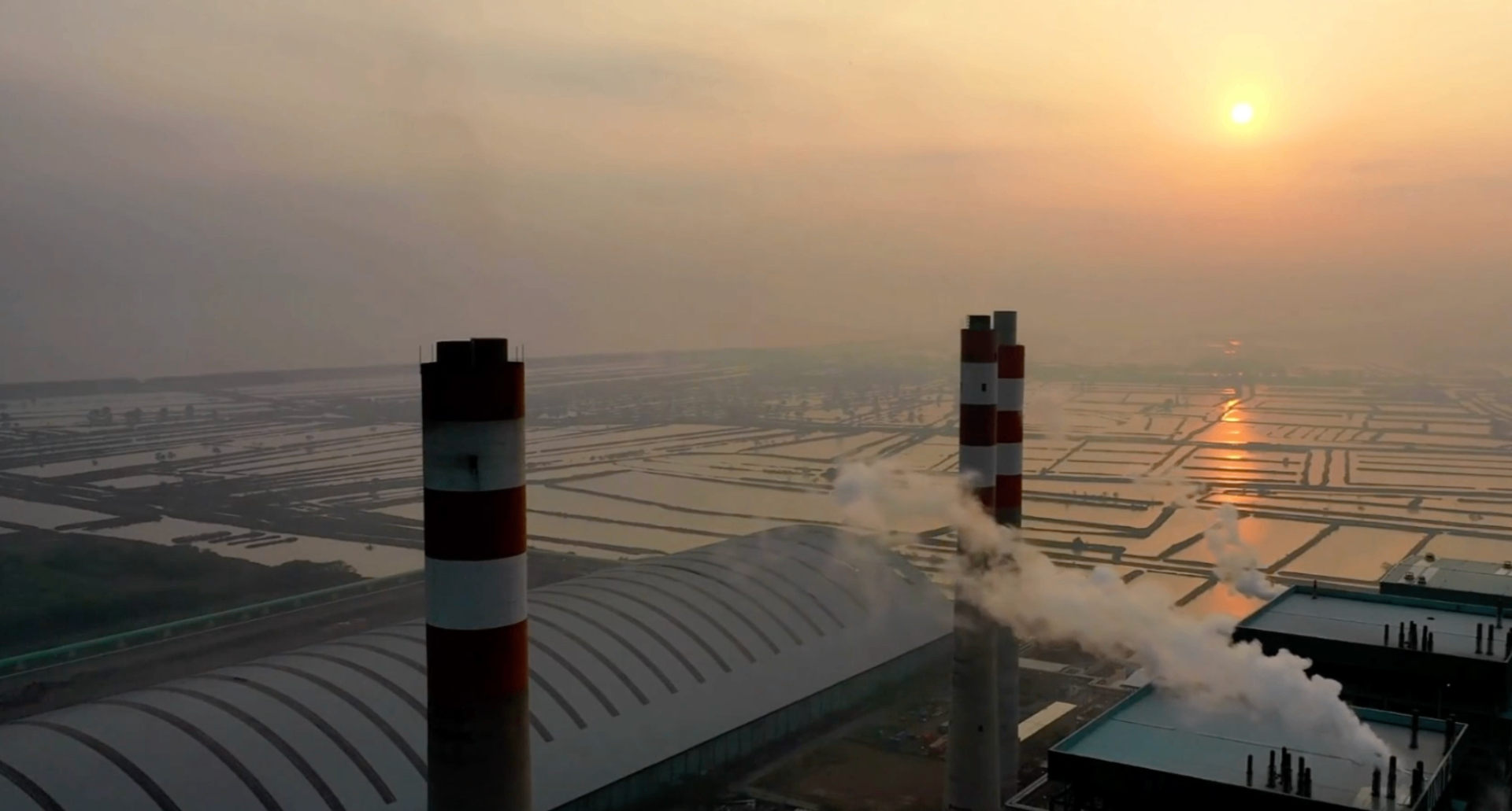 Aerial view of an industrial waste and energy facility at sunset, chimneys over a vast grid of basins.