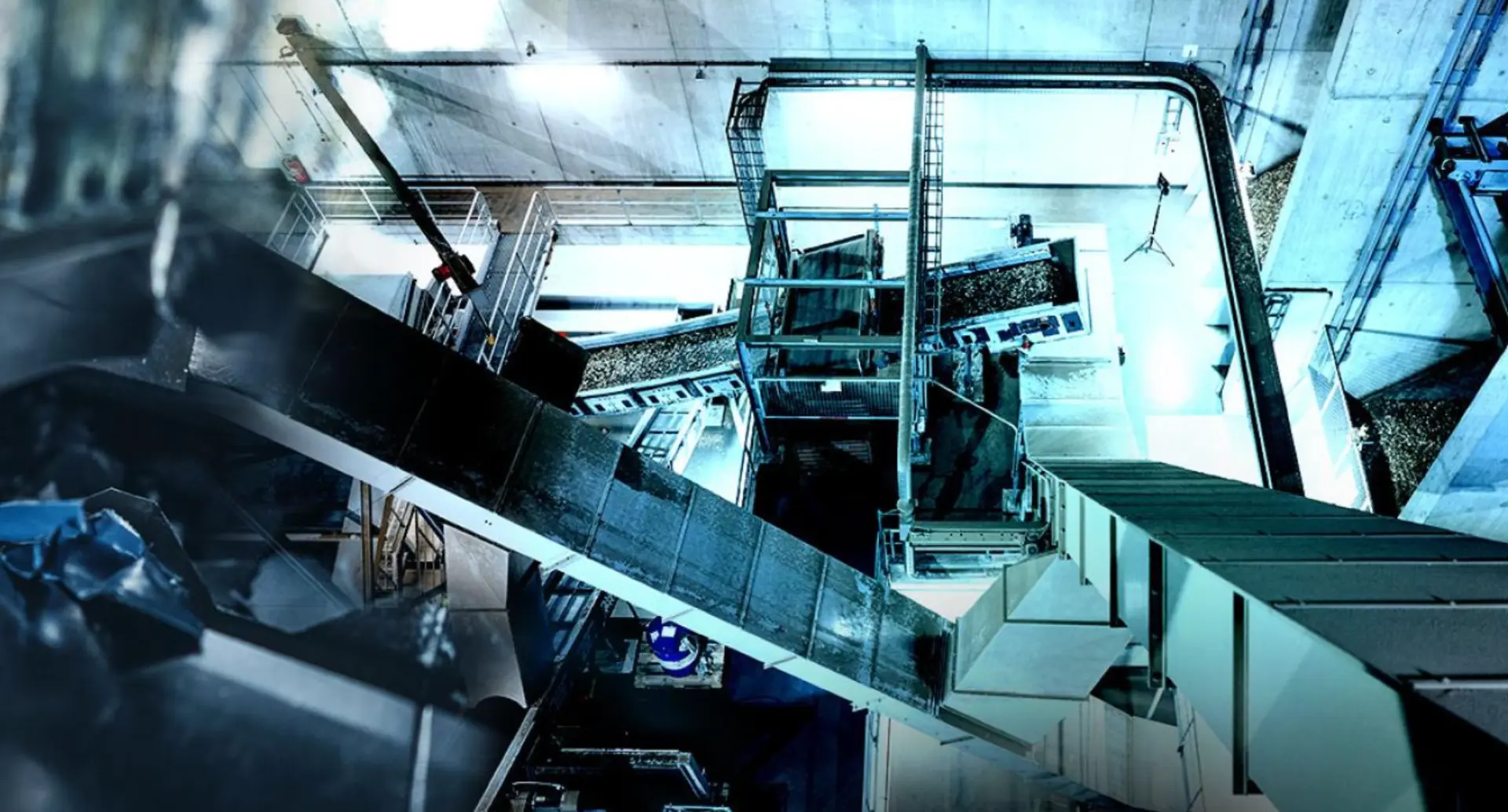 Interior view of an industrial waste facility with conveyor belts, sorting machinery and concrete structures under cool lighting.